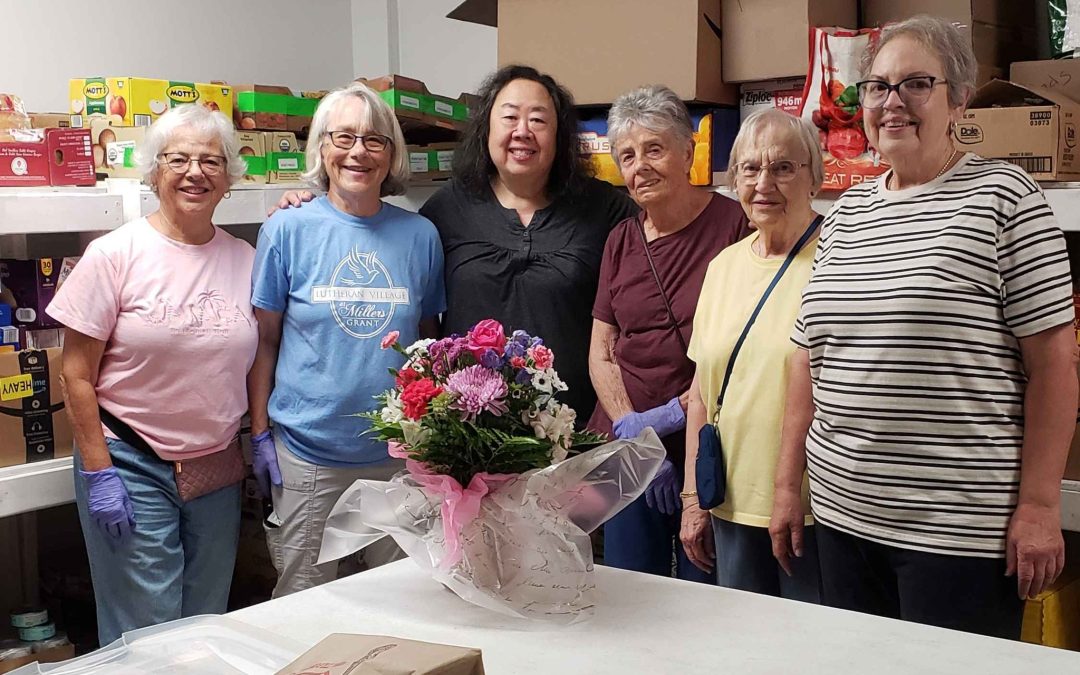 a group of volunteers from Millers Grant pose with a site coordinator from CCC. A bouquet of flowers sits on a table in front of them.